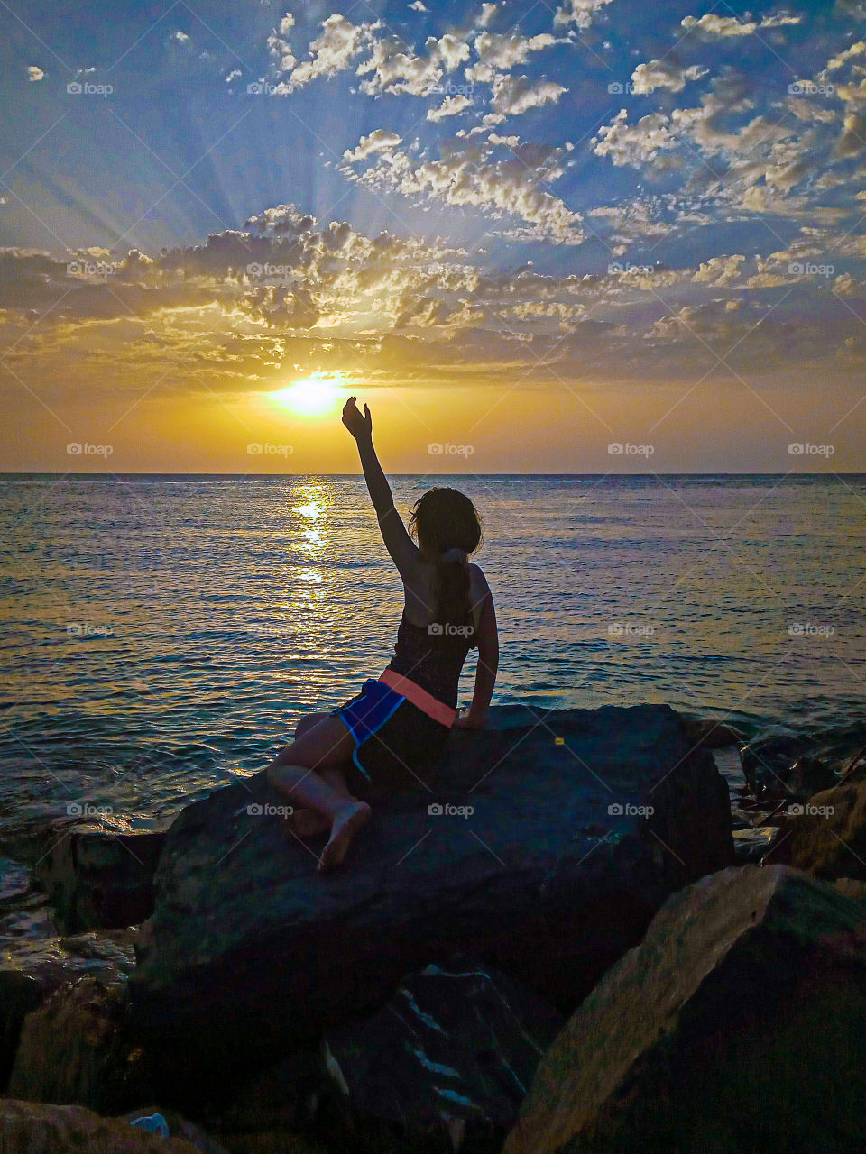 a little girl trying reach the sun at sunset