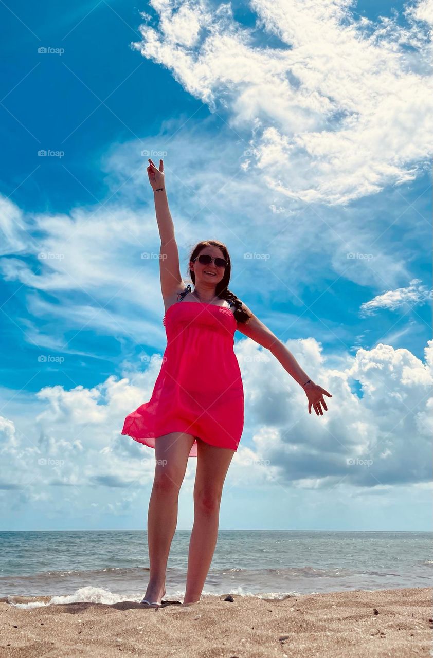 A young woman hanging out on the beach on a warm summer day with a neon pink coverup and green bathing suit