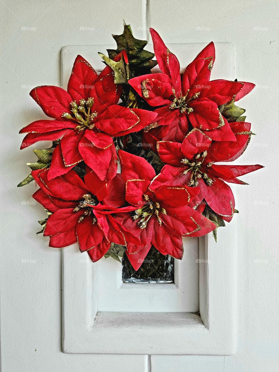 Christmas wreath made of artificial poinsettias, the Christmas flower, hanging on a white front door.