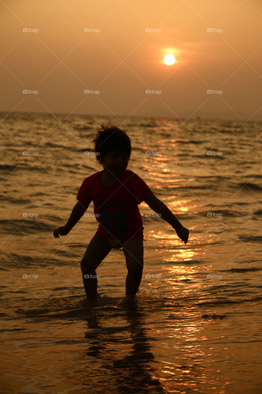 Young boy surfing on the beach during sunset 