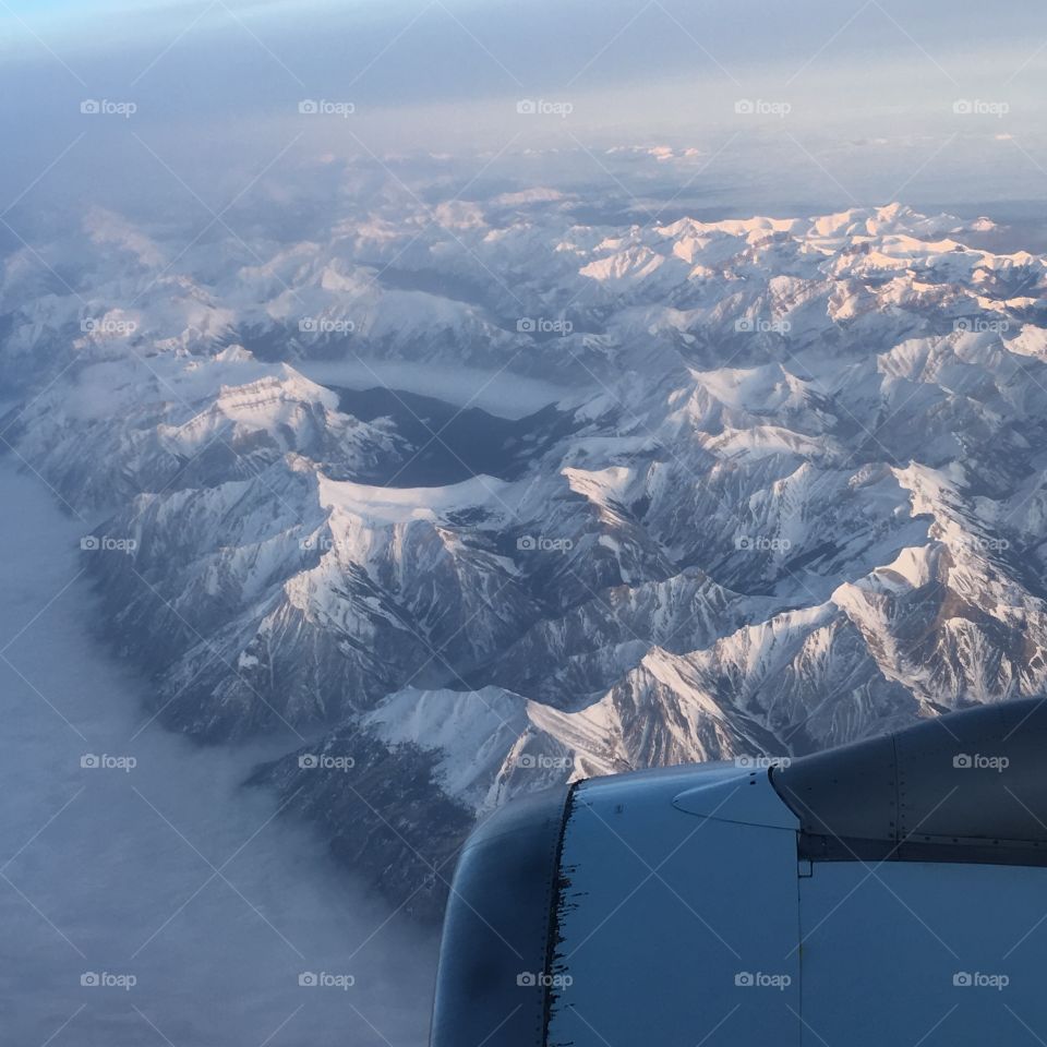 flying over snow capped rocky mountains in an airplane