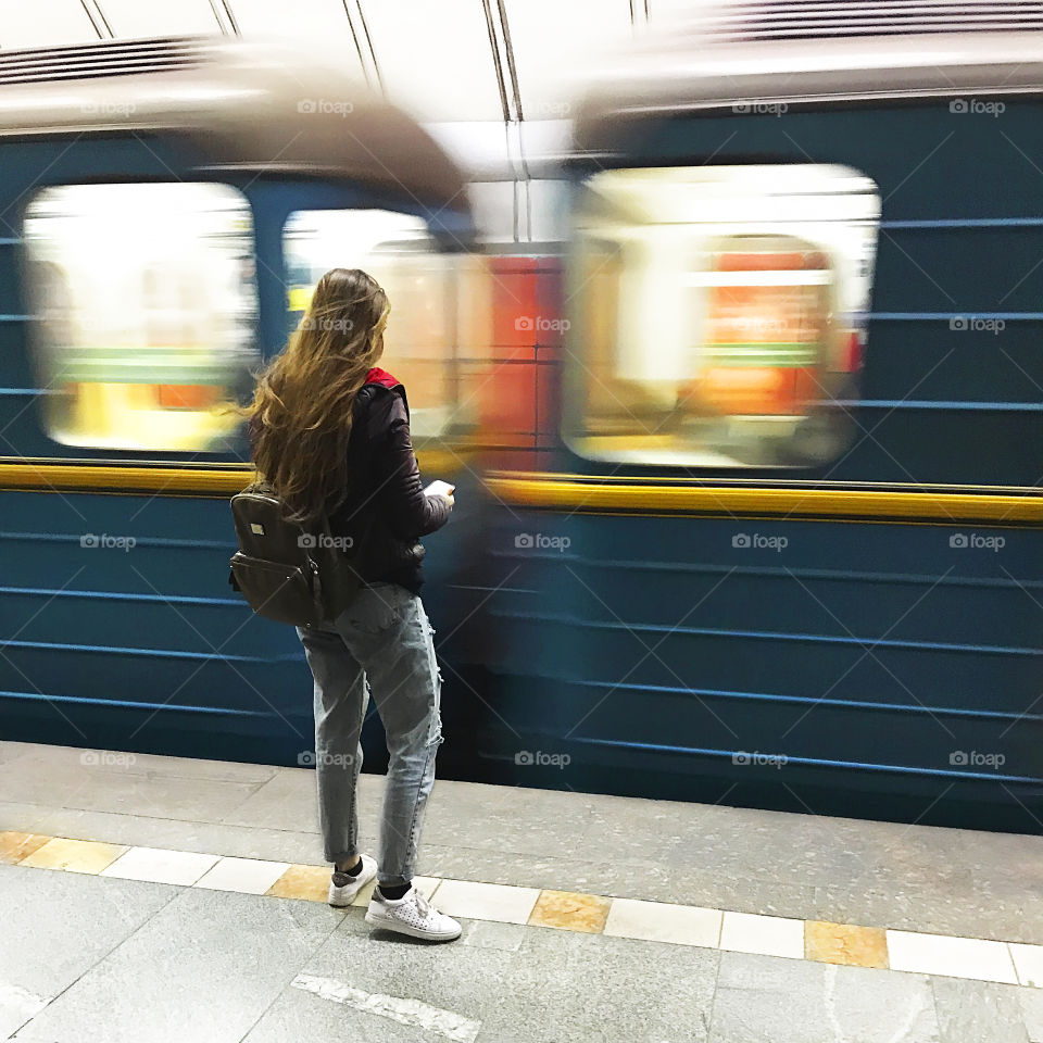 Young woman with a backpack and a mobile phone waiting for a train while traveling through the city 