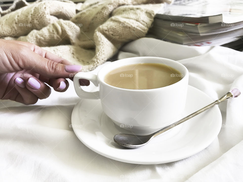 Young woman drinking coffee in cozy bed with sweater 