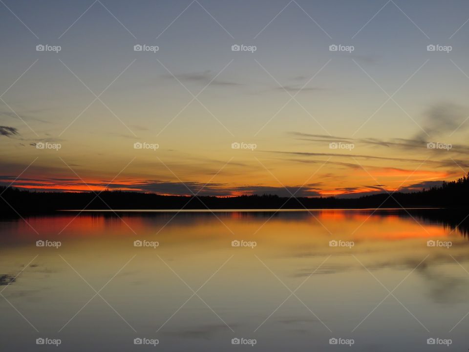 An orange, cloudy sunset reflected in the calm waters of the Little Current River in northern Ontario, Canada. 