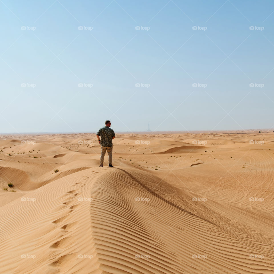 Alone in the desert. A man in light clothing walks through the desert. Golden sand dunes and blue sky. Travel destinations