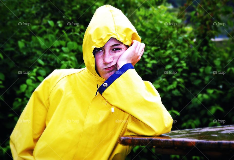 What a bad weather. Girl in a yellow raincoat with frustrated  facial expression on a rainy day