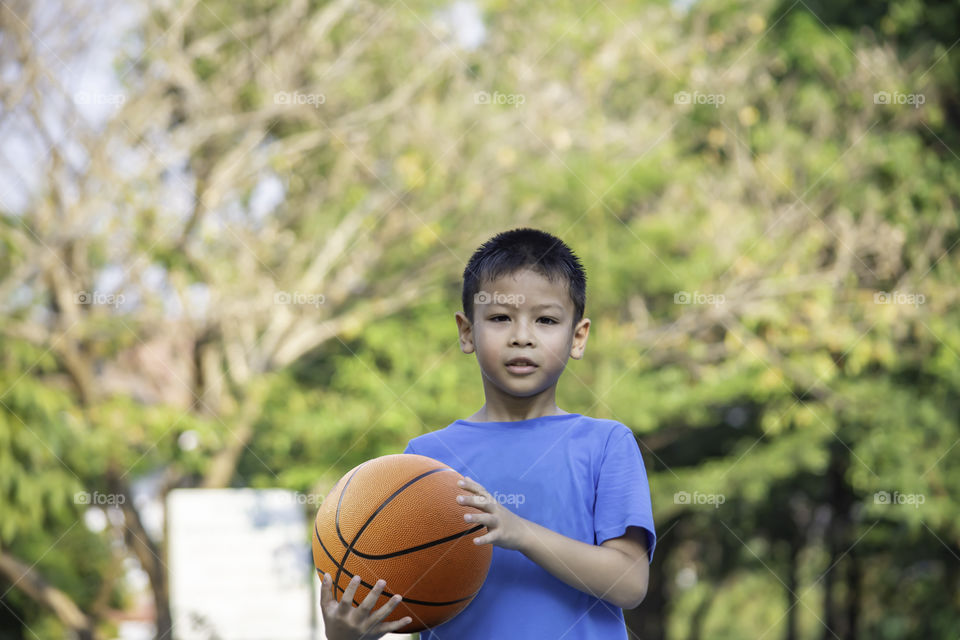 Asian boy holding a basketball ball Background blurry trees.