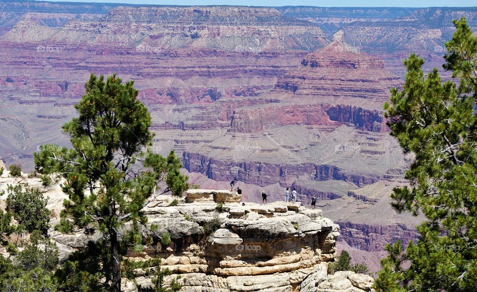 People hang precariously from a rock outcropping at the Grand Canyon