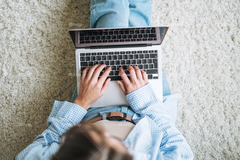 Crop photo of young woman in jeans working on laptop sitting on carpet at home, view from top