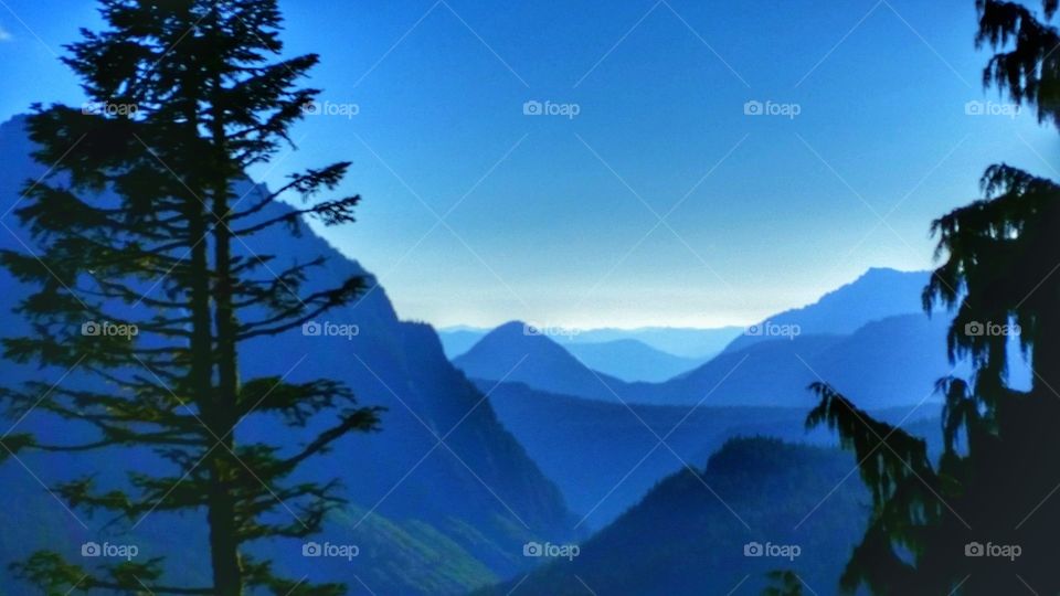 Beautiful and blue colored mountains surrounded by valleys, hills, terrains and plateaus with trees on the sides.