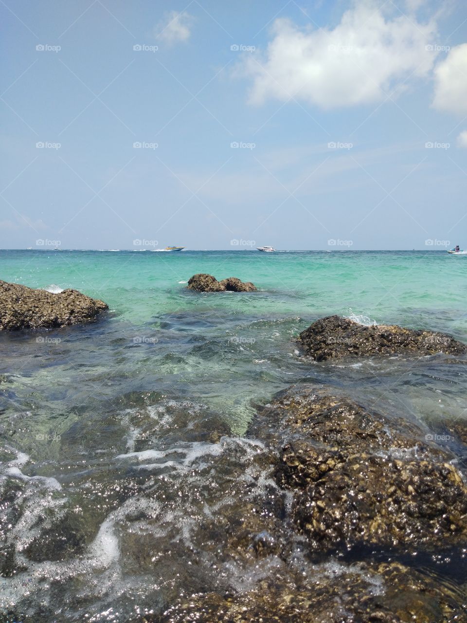 The beautiful sea view consisting of clear waters, rocks, bright skies, white clouds and  sunlight.