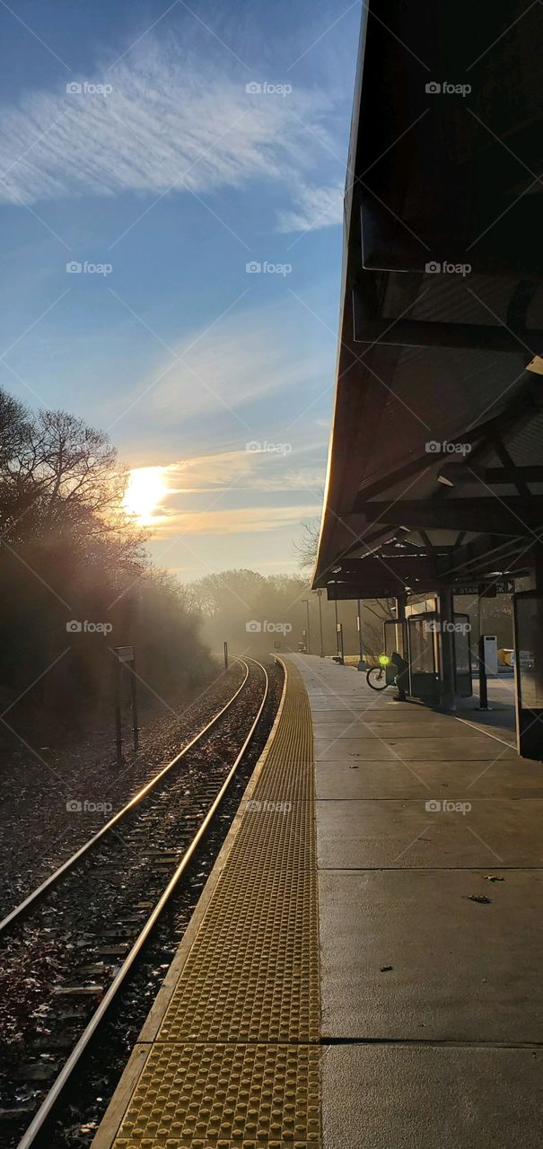 Waiting for commuter train on platform before other people gather. Blue sky & fog around the corner bend.