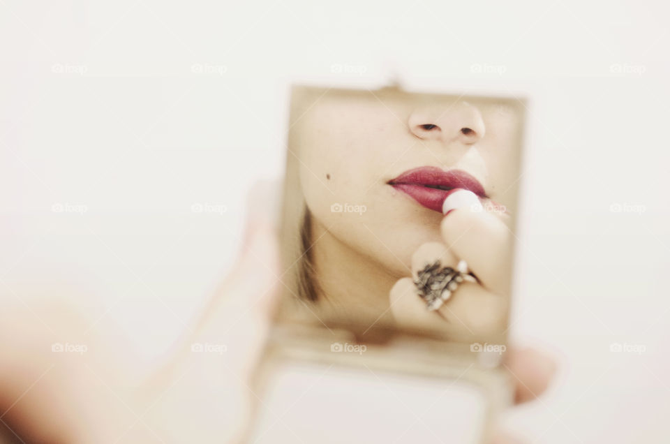 Woman in front of a mirror putting lipstick on 