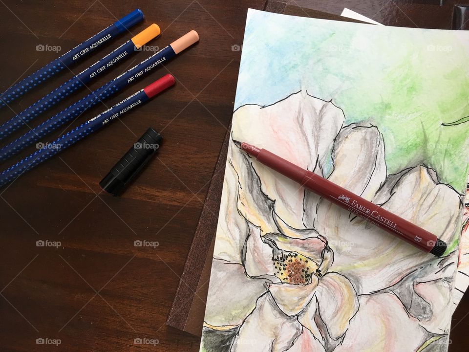 Flat lay Watercolor sketch of flower on Wood table and sketchbook with colorful Faber-Castell PITT Artist pens and Art Grip Pencils 