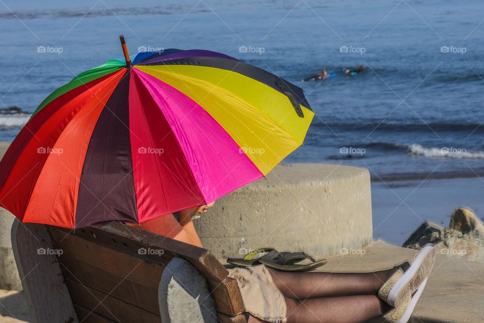 Beautiful vibrant rainbow colored umbrella being used to provide shade from the sun while relaxing at the beach in Capitola California