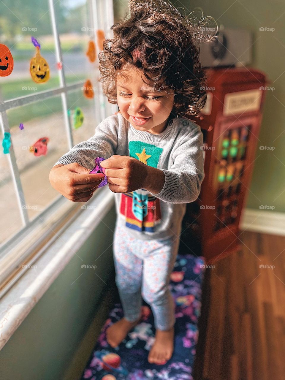 Child hanging Halloween decorations, child laughing while decorating for Halloween, toddler girl laughing while holding a purple skull decoration, toddler girl helping decorate 