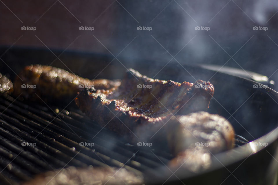 A delicious portrait of some barbecue meat cooking on the grill of a charcoal barbecue.