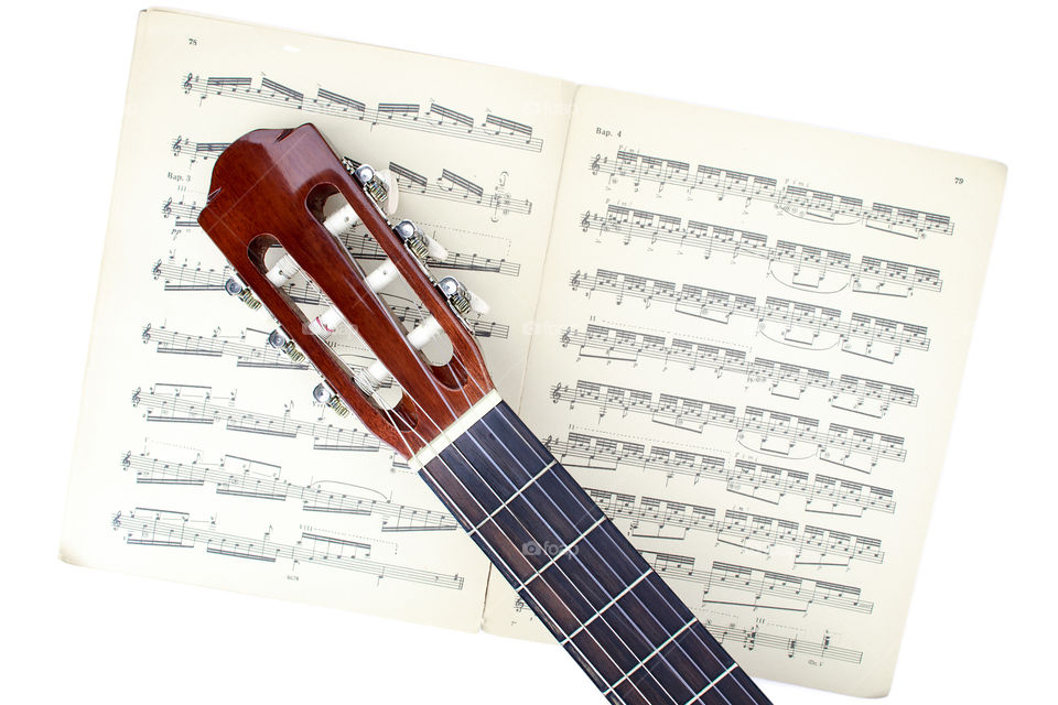 Guitar lying on a book with notes (white background)