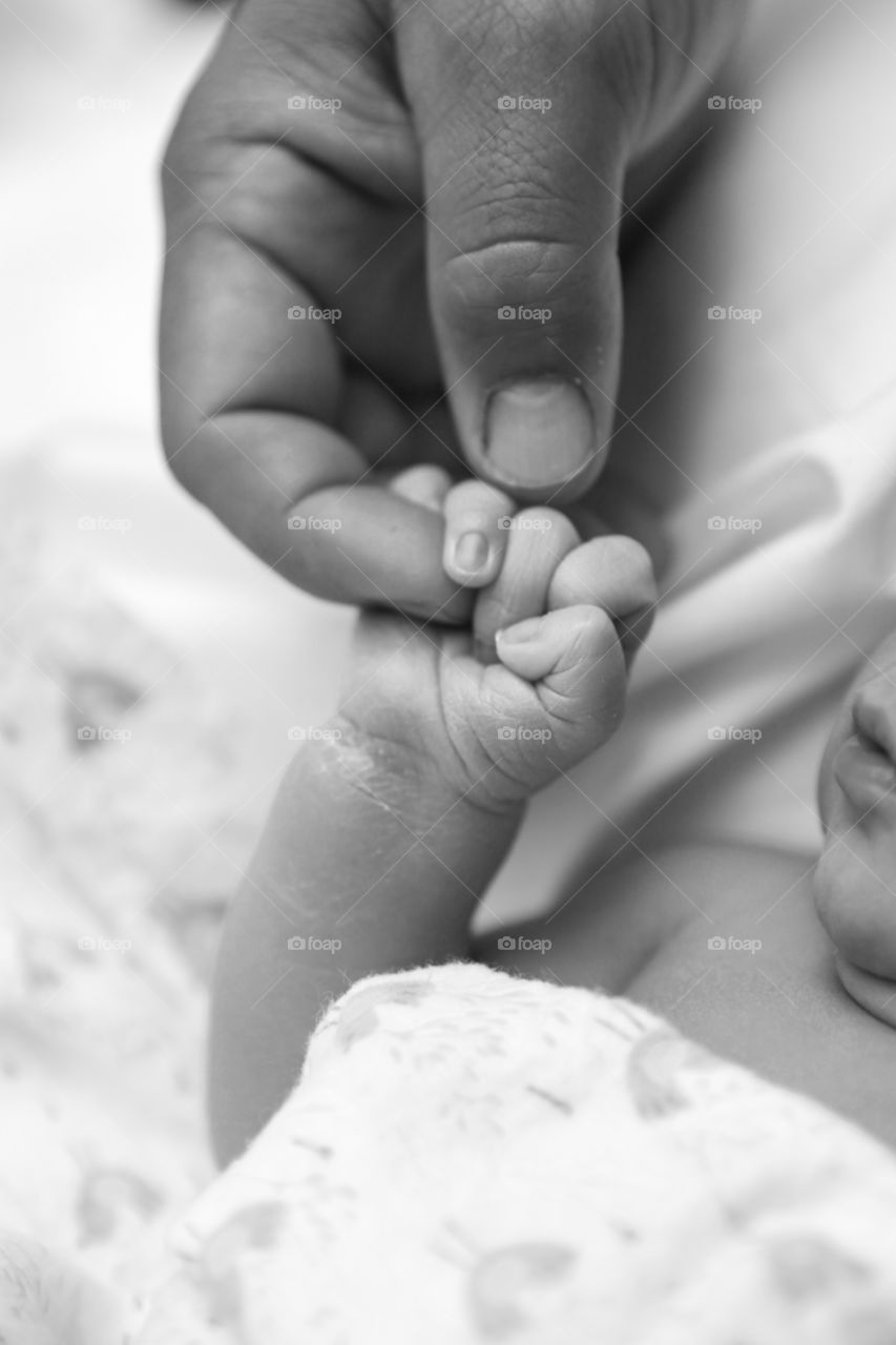 A little baby holds the finger of his dad with his whole hand