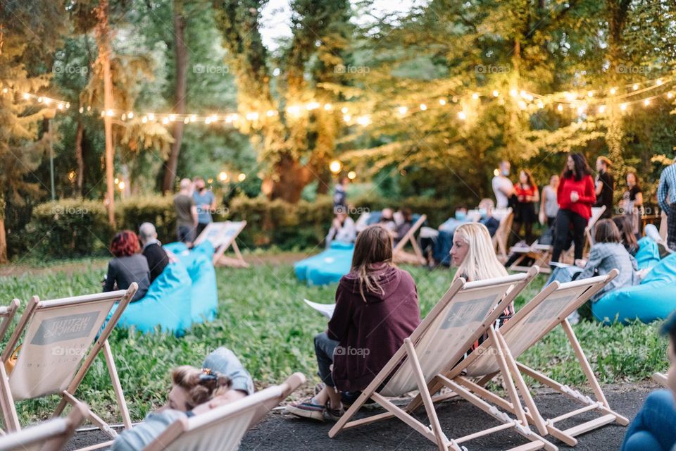 Two women talking, while being at a movie night at a public garden in the city. 