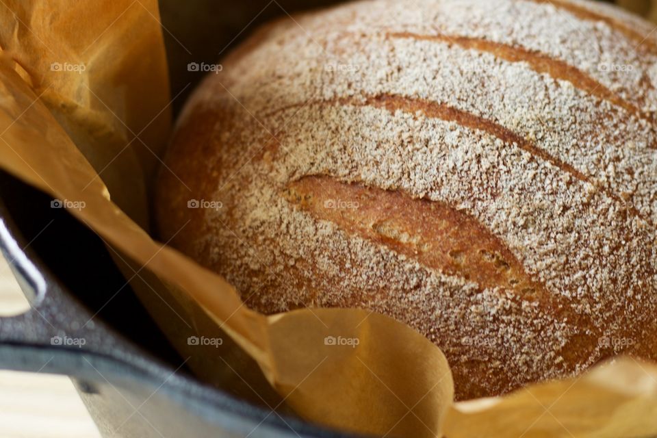 A freshly baked round loaf of sourdough bread on parchment paper in a cast iron Dutch oven