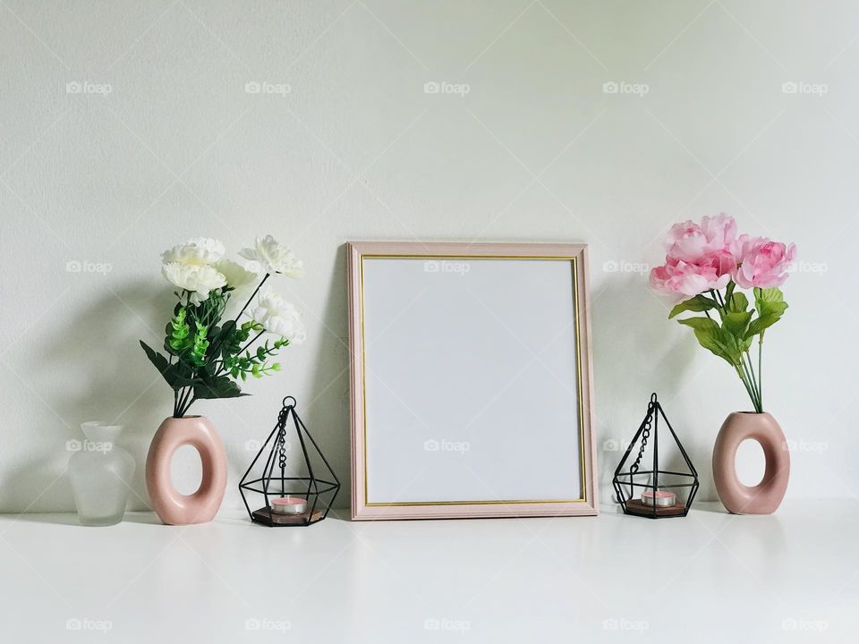 A pink colour photo frame along with pink and white flowers in pink flowers vases and pink candle in candle holder on white table looks pretty 😊