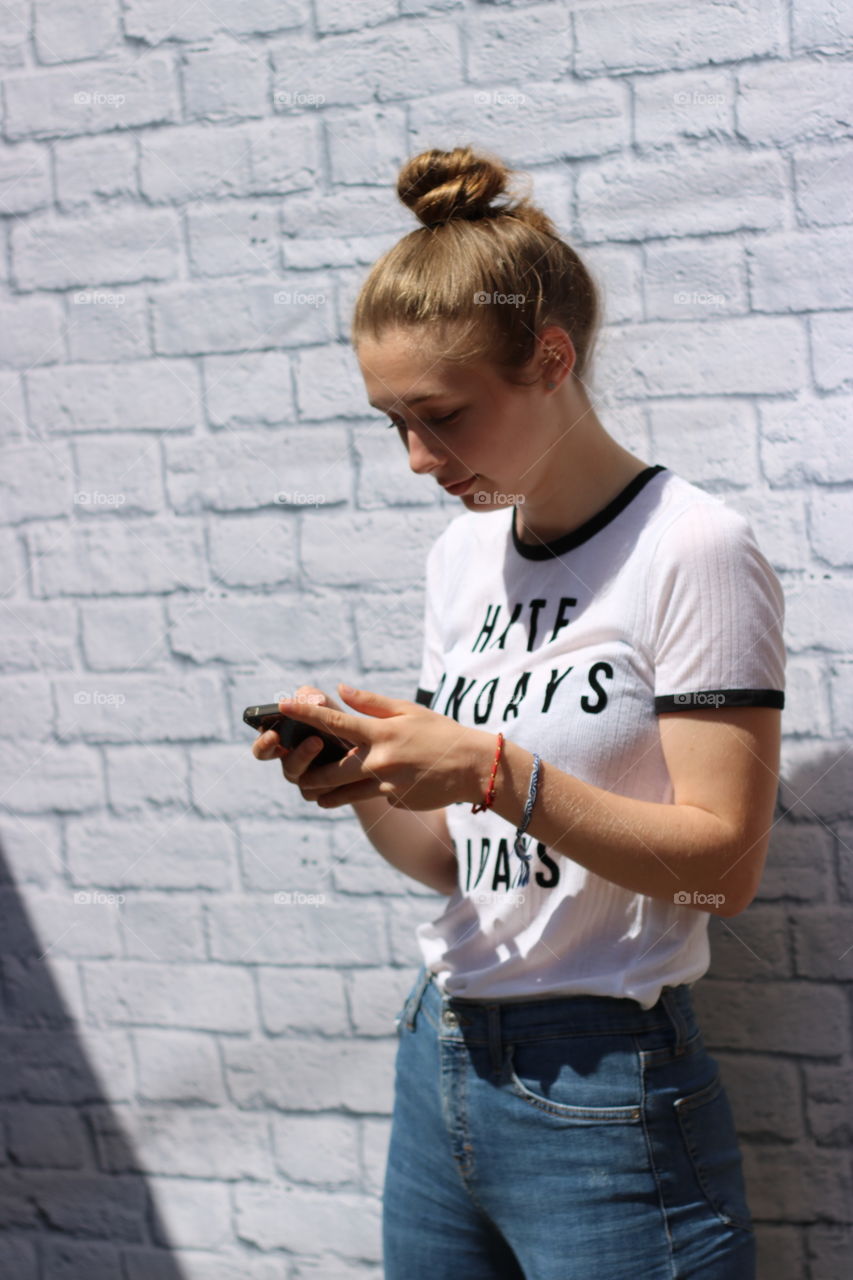Young girl using mobile phone against wall