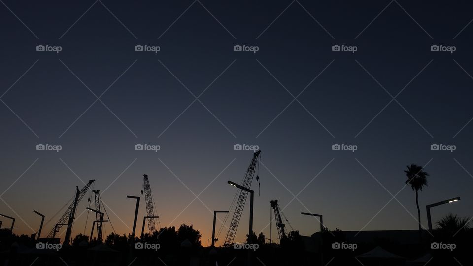 Silhouettes of construction site at the time of dawn. Many cranes can be seen there.