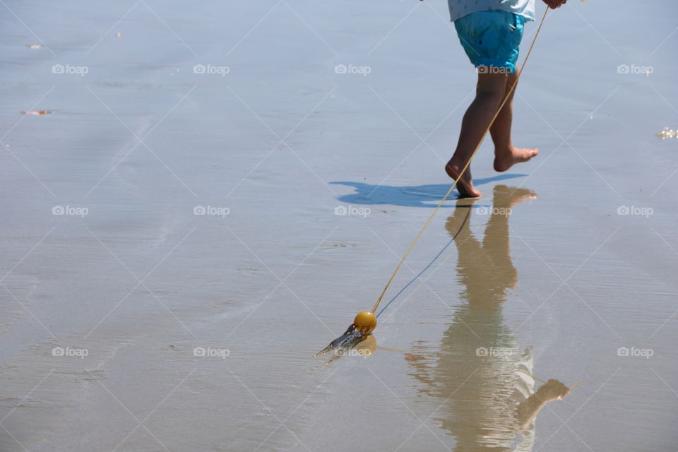 Boy running in a shallow water , playing with kelp .. it’s reflection following him..