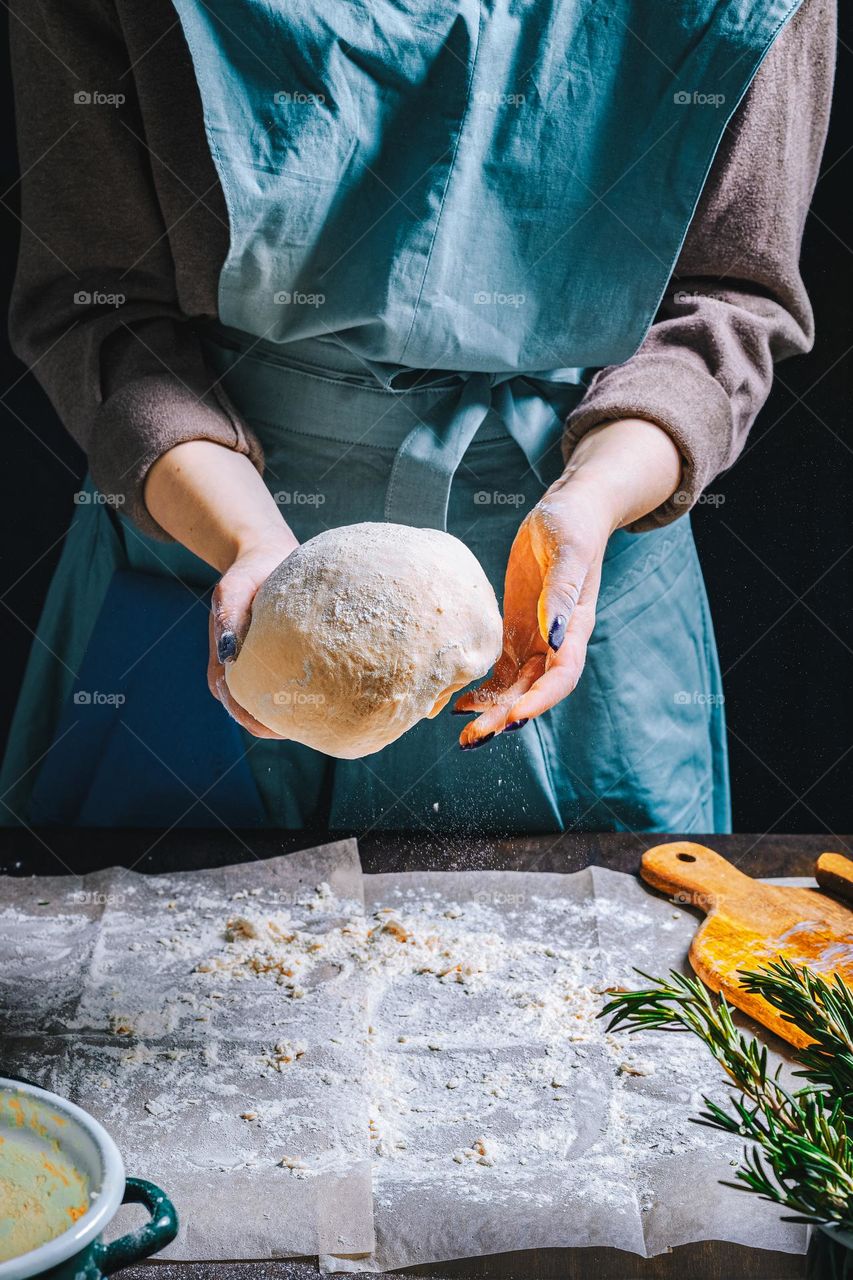 Women's hands, flour and dough. Levitation in a frame of dough and flour. A woman in an apron is preparing dough for home baking. Rustic style photo. Wooden table, wheat ears and flou.Emotional photo