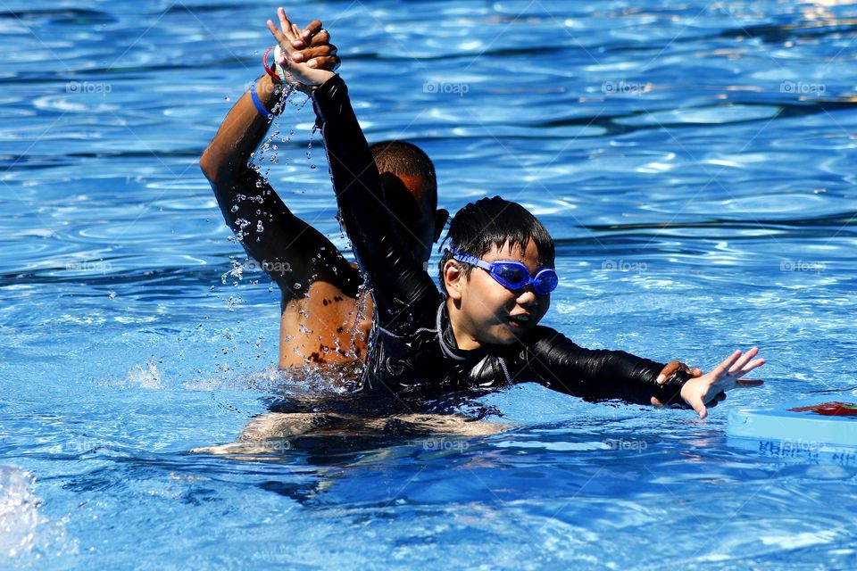 young kid learns how to swim with the help of a swimming coach