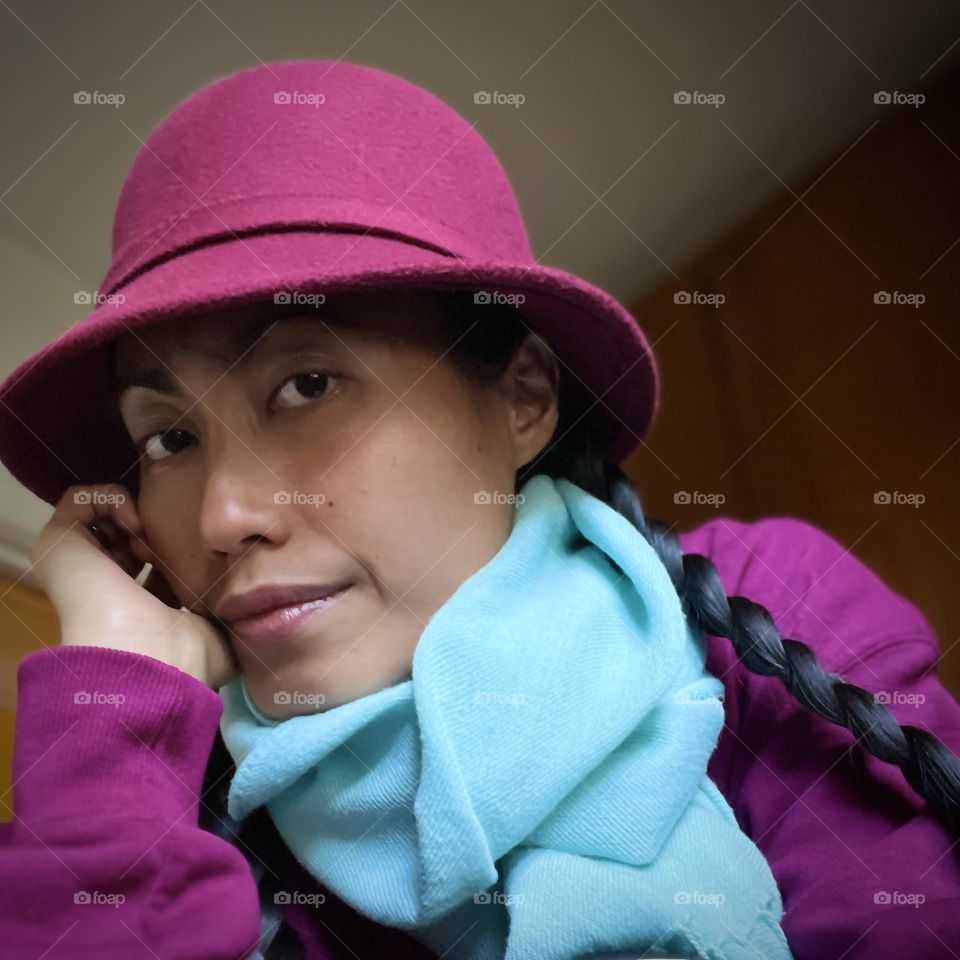 Young woman wearing magenta sweater and a hat with light blue scarf.