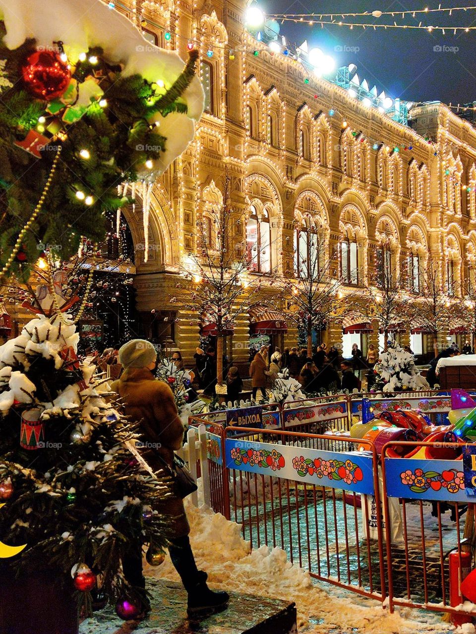 December 2021. Red Square of the Kremlin. Evening. The GUM building in luminous garlands, people walking, a decorated Christmas tree, an attraction. Everything is covered in snow. Moscow