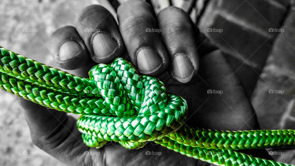 Mão com nó de cordas verdes.