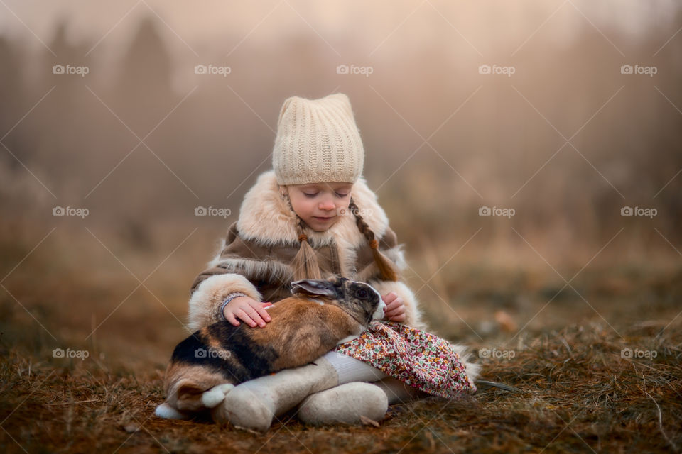 Cute Little girl with bunny in a forest at misty autumn evening 