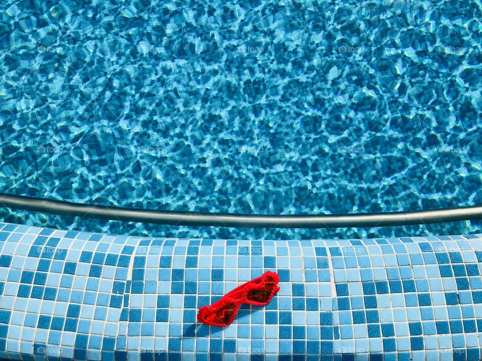 Heart shaped sunglasses on the edge of a pool with turquoise water