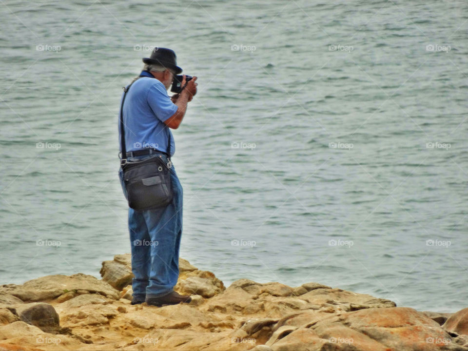 Old man shooting photos by the sea