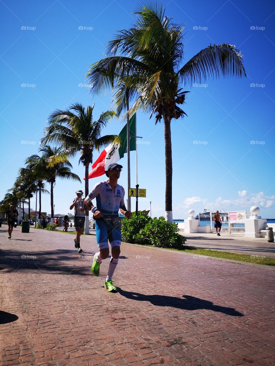 atletas corriendo triatlón denominado iron man en la isla de Cozumel peleando por ser un iron Man, última etapa y de fondo la hermosa bandera de México