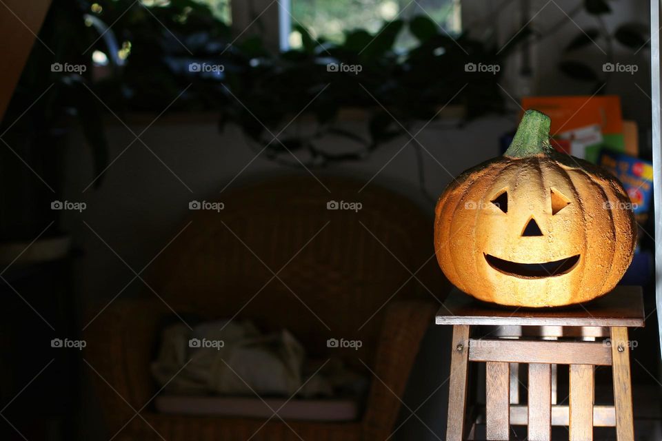 An orange decorative pumpkin stands on a brown wooden shelf and is illuminated by the sun in living room 