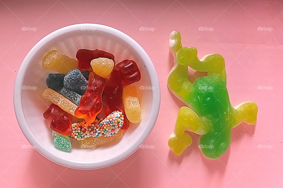 Candy display of a variety of bright and colorful gummy bears, sour patch kids and a giant bright green and yellow frog sitting on a pink background display