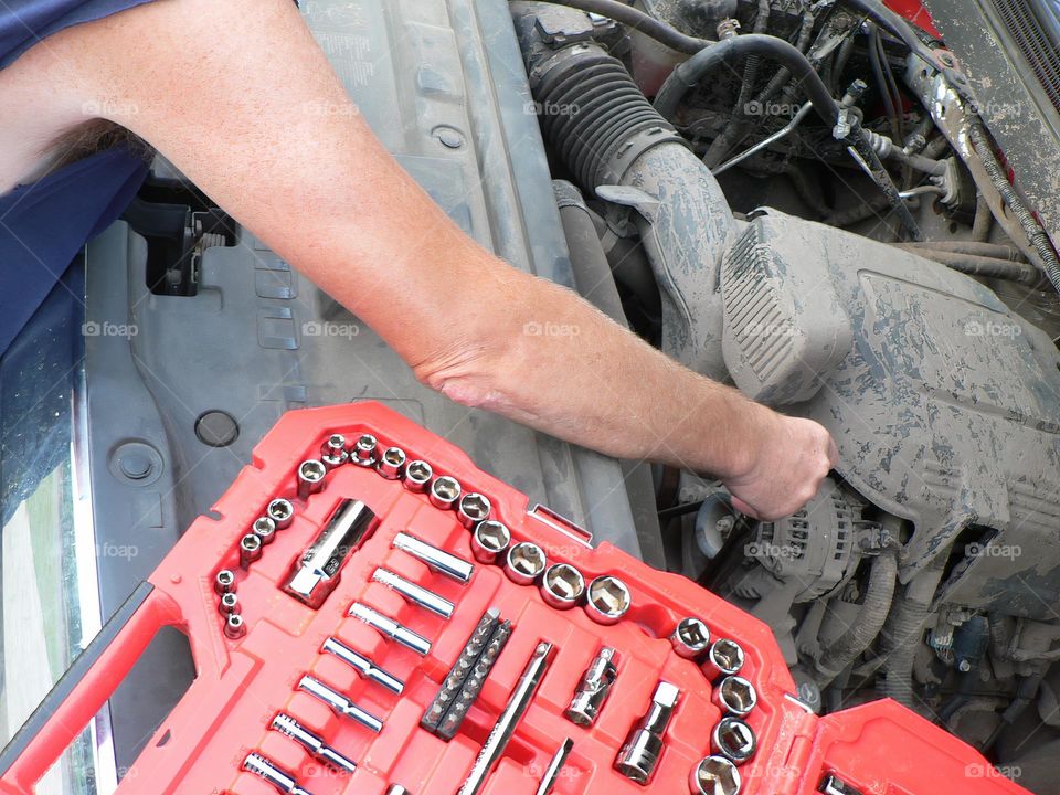 Under the hood of a red pickup truck with combination wrench set tools organized in a red tool hard case by the work station and the mechanic handyman fixing a piece.