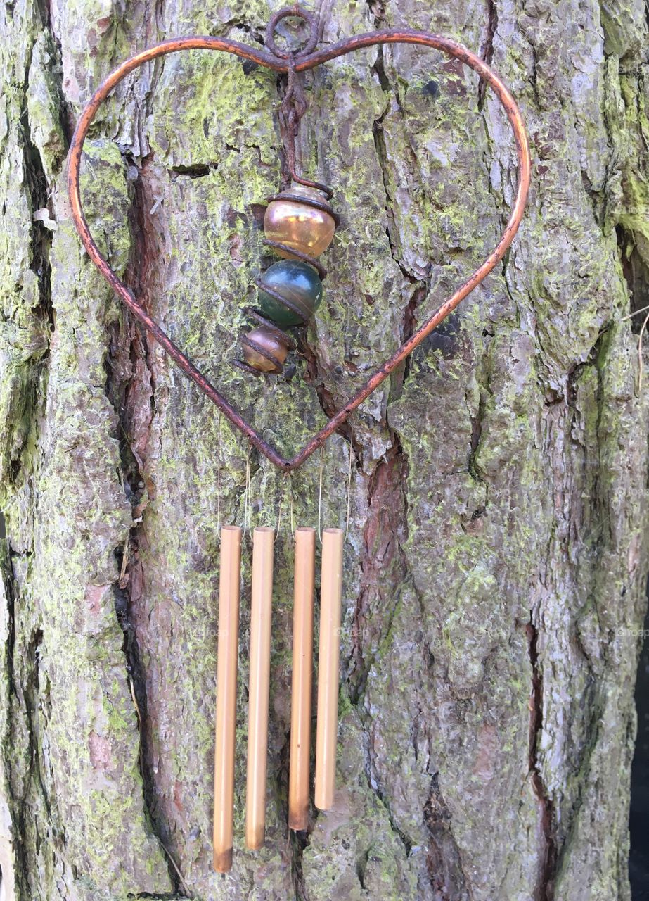 Hanging copper heart wind chimes on a pine tree trunk