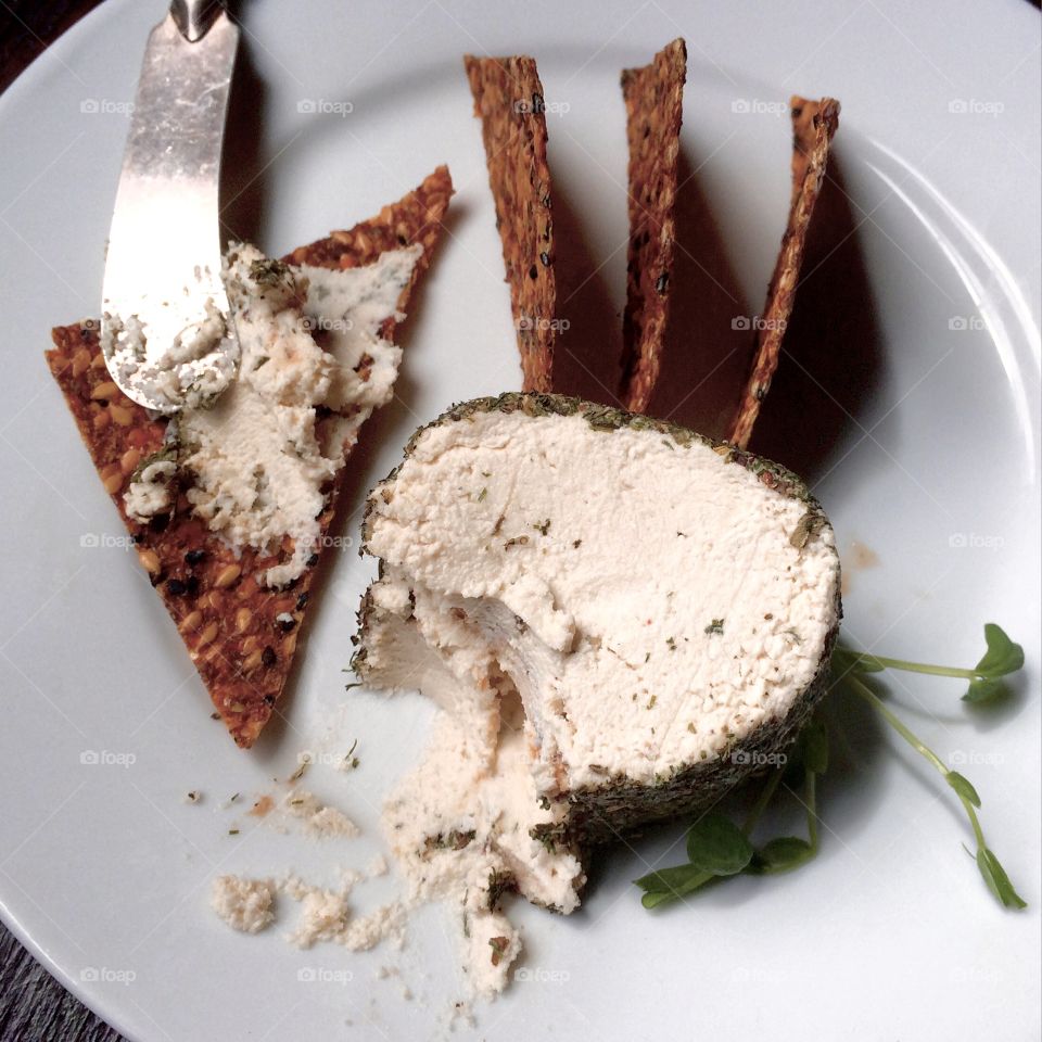 Herbed cashew cheese with raw flax crackers on a white plate with cheese knife.