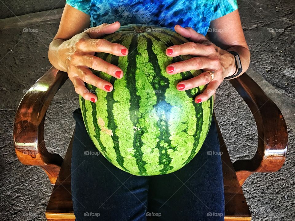 Holding watermelon on lap with red nails.