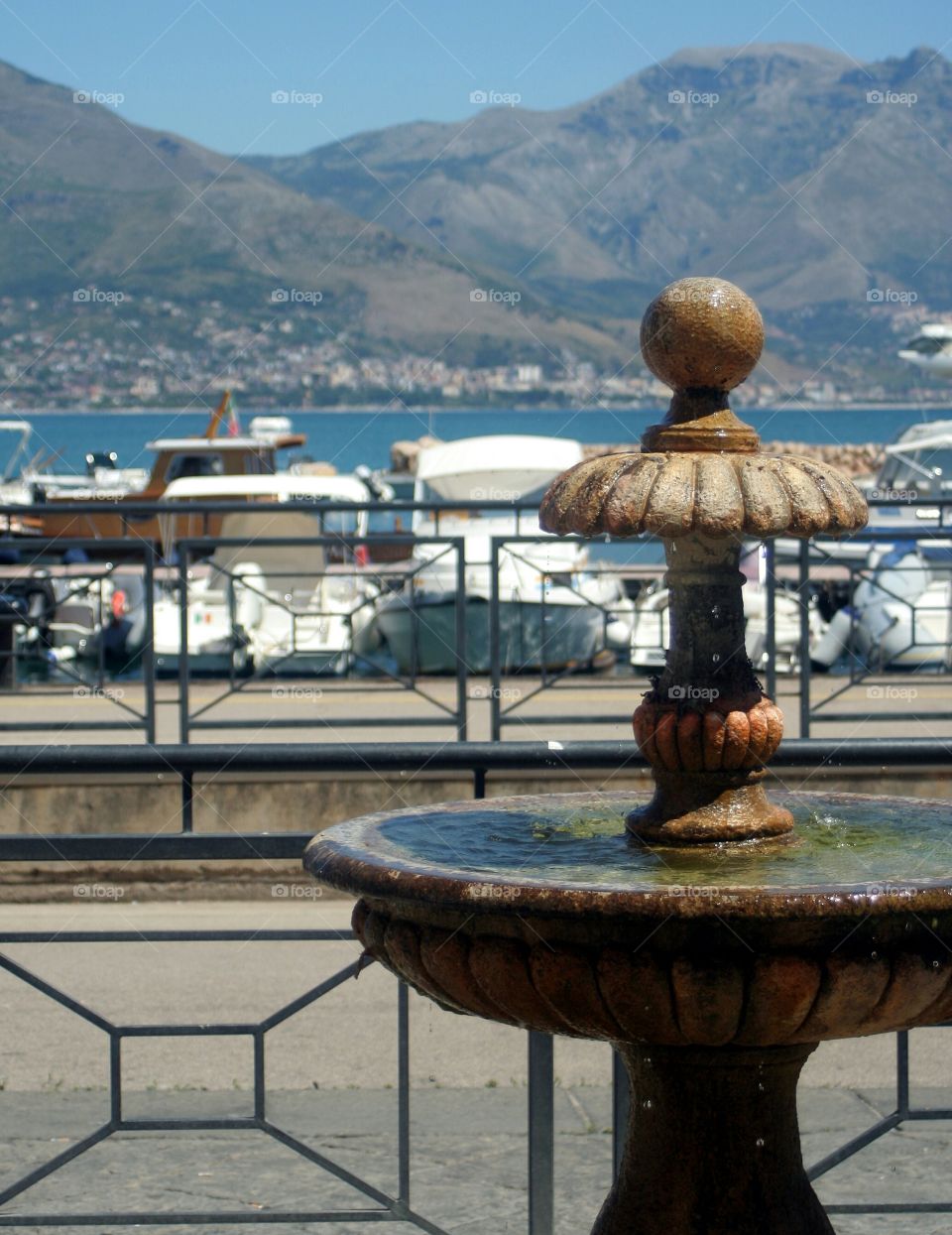 Water drops from a tiny fountain; sea and little boats on background.