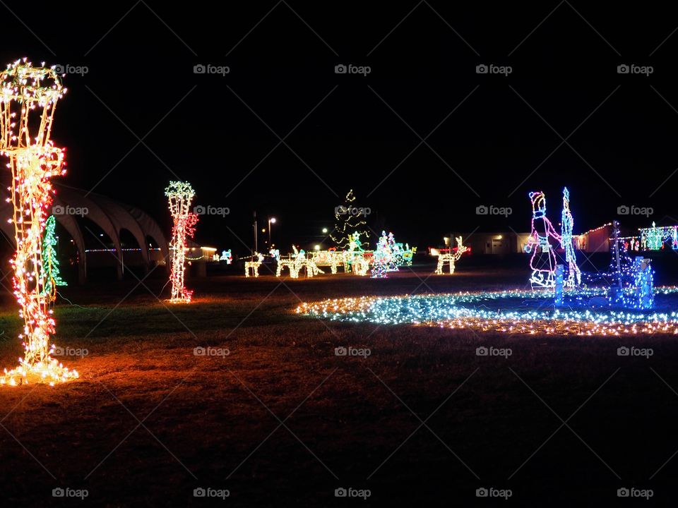 A beautiful outdoor Christmas light display after dark with decorated poles and ice skaters.