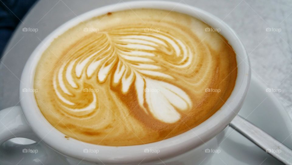 A closeup cup of cappuccino,  with a floral pattern on the froth.