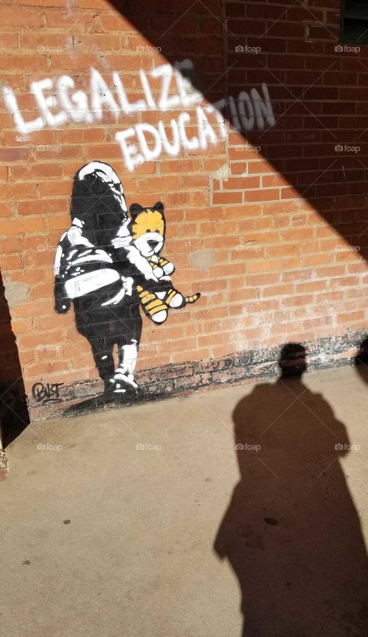 Graffiti art of figure carrying bear on red brick wall with shadow watching.