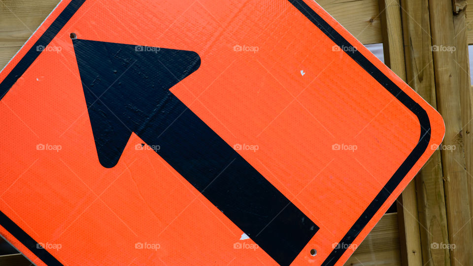 Orange arrow on street sign or road construction sign closeup on wood background abstract direction photography 