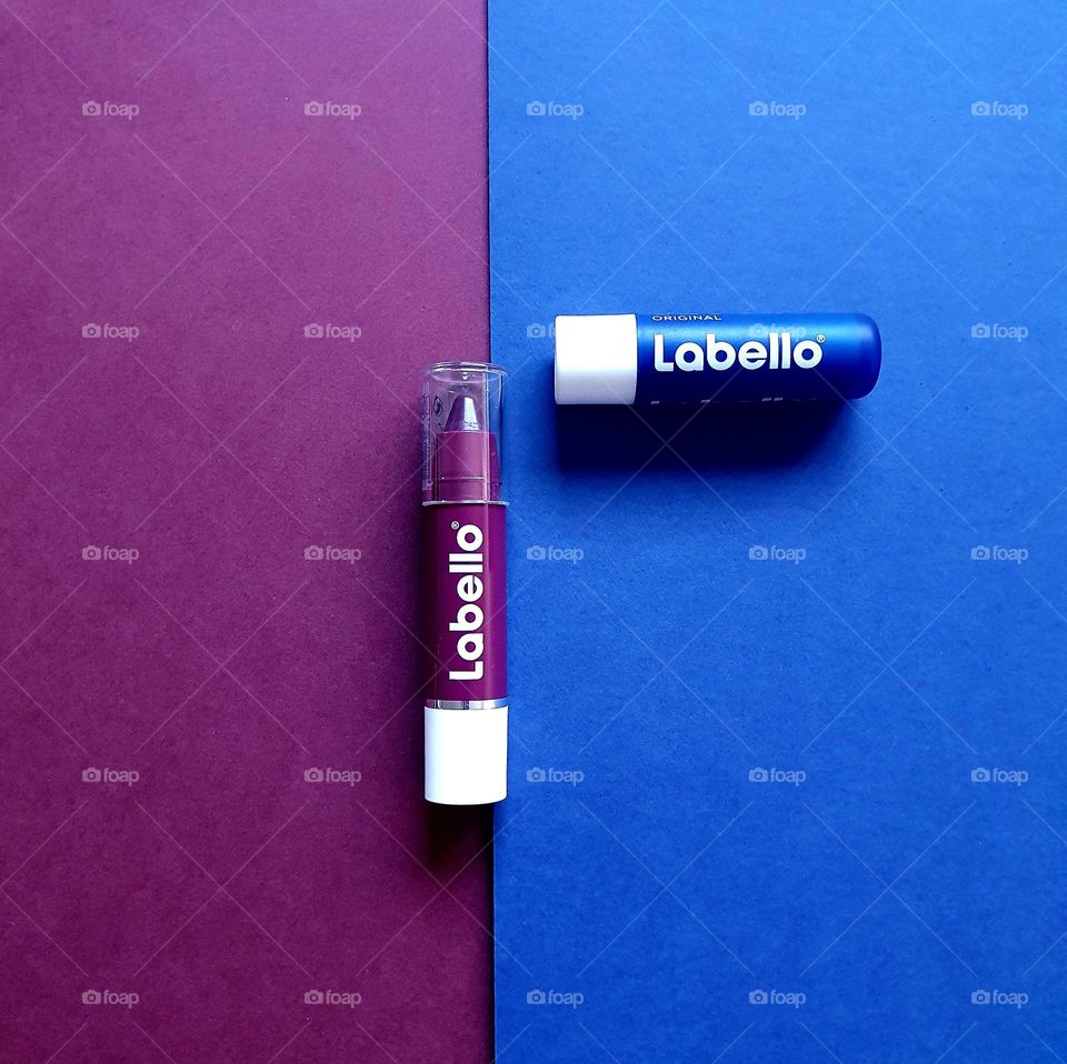 Flatlay on plum and navy blue papers of Labello black cherry crayon and Labello original